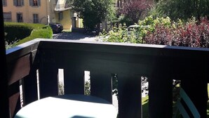 Een balkon met een tafel en stoelen, met uitzicht op een berglandschap met gebouwen en groen.