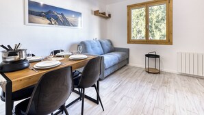 Een eetgedeelte met een houten tafel voor vier personen, een grijze bank en een raam met uitzicht op bomen.