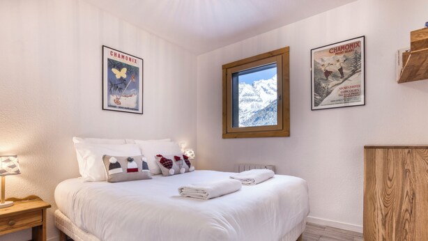 Een slaapkamer met een groot bed, een houten nachtkastje, een houten dressoir en twee posters aan de muur.