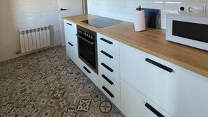 Een moderne keuken met witte kastjes, een ingebouwde oven, een magnetron en een houten aanrecht.