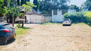 A parking area with two cars, a building with a sign, and a fence. - Enjoyable bed & breakfast in charming Diani near the beach (DIANI)