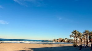 Una spiaggia con cielo sereno, palme e un edificio sullo sfondo.