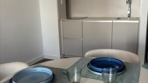 Una cucina compatta con forno a microonde, lavello e pensili. Si nota un tavolo con due piatti blu e due bicchieri.