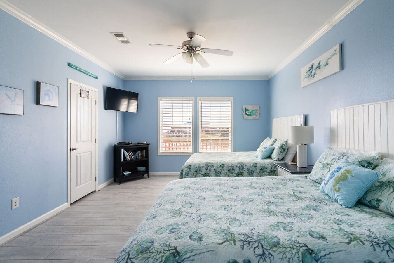A bedroom with two beds, a ceiling fan, a TV, and a bookshelf.