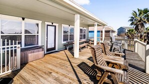A wooden deck with outdoor seating, a covered area with windows, and a view of neighboring houses. - Family Haven with Fireplace, Garage hangout, and pet friendly (Bolivar Peninsula)