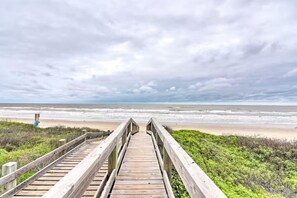 En träpromenad som leder till en strand under en mulen himmel.