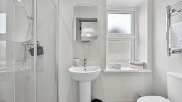 Un baño moderno con ducha de vidrio, lavamanos pedestal, espejo y ventana.