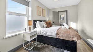 A modern bedroom with a bed, bedside table, lamp, and artwork on the wall. - Cosy Flat in City Centre (Cardiff)
