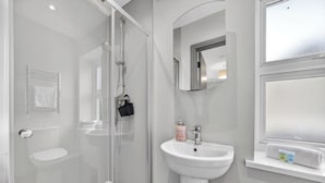 A modern bathroom with a glass shower enclosure, a white sink, and a mirror above it. - Cosy Flat in City Centre (Cardiff)