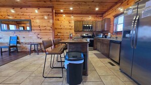 Una cocina con paredes de madera, un refrigerador de acero inoxidable y un comedor con mesa y sillas.