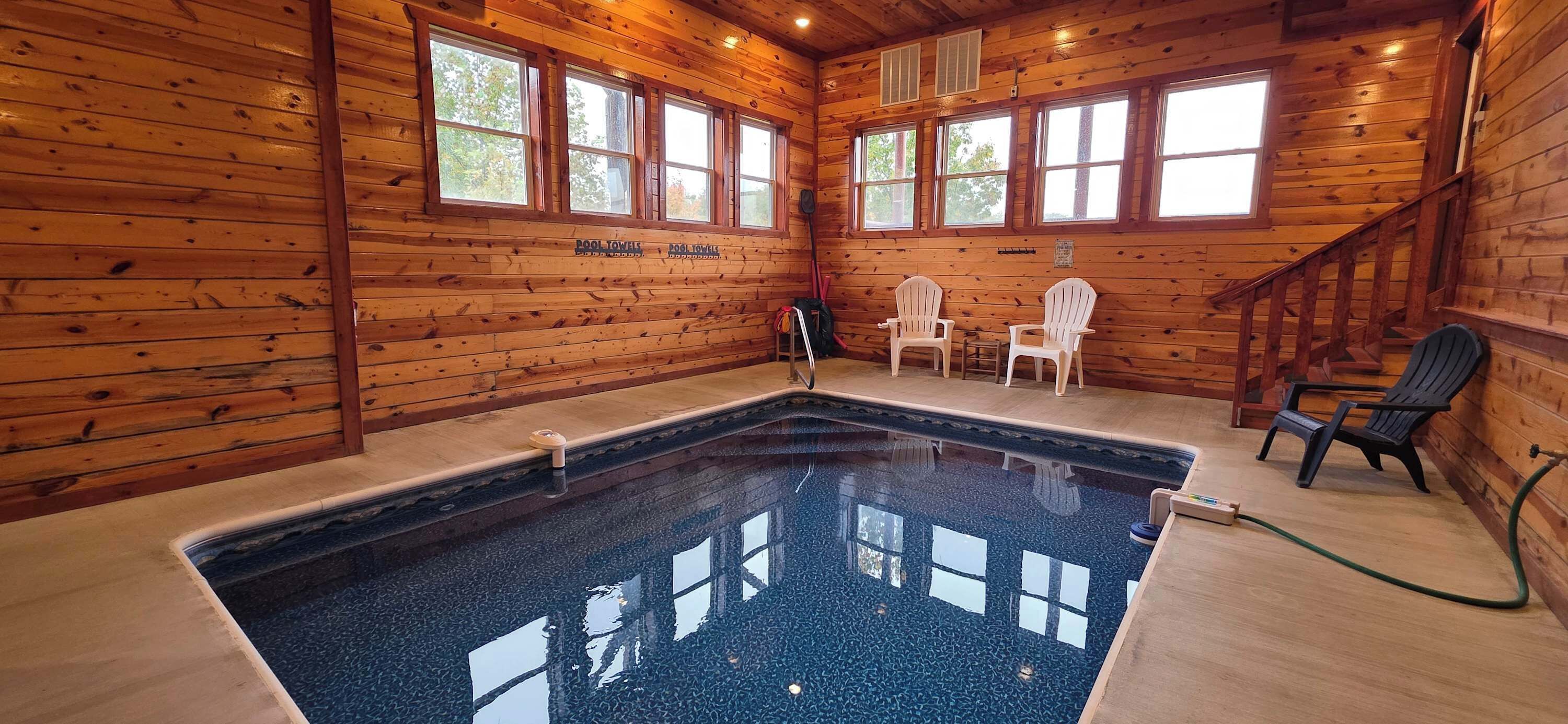 Interior de una cabaña de madera con piscina, paredes de madera y una escalera.