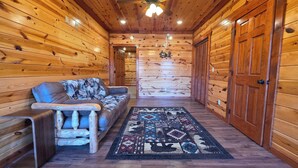Interior de una cabaña de troncos con un sofá, un tapete estampado y paredes de madera.