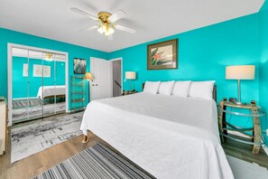 A bedroom with a large bed, a ceiling fan, and a teal-colored wall. - Laguna Beach Breeze (Panama City Beach)