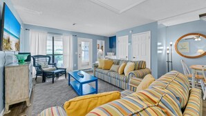 A living room with a striped sofa, a blue coffee table, and a wicker chair. - Laguna Beach Breeze (Panama City Beach)