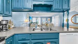 A kitchen with blue cabinets, a stainless steel sink, and a coffee maker. - Laguna Beach Breeze (Panama City Beach)