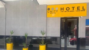 A hotel entrance with a yellow sign, potted plants, and a reflection of a red car in the glass door. - Unity Hotel - Santos (Santos)