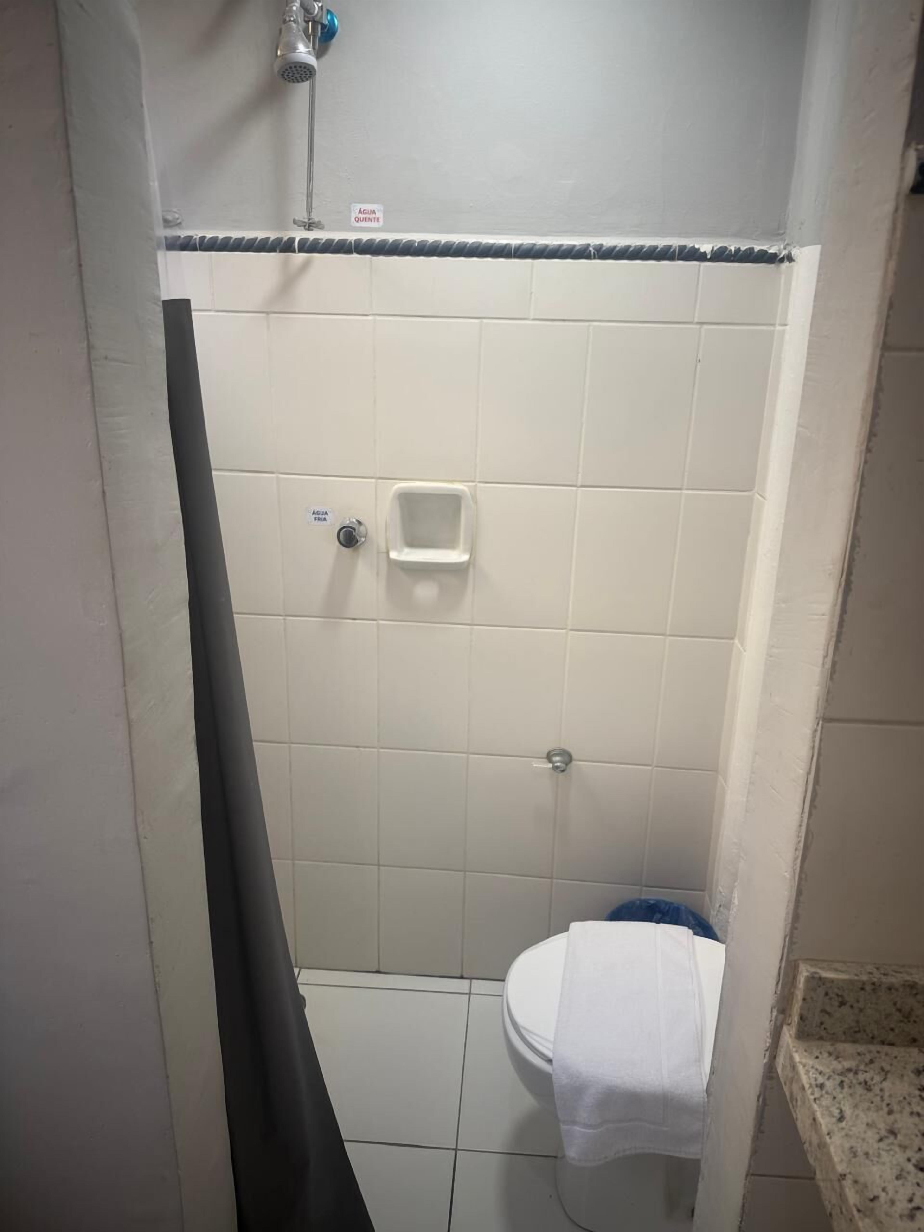 A small bathroom with white tiles, a shower, a toilet, and a towel hanging on the wall.