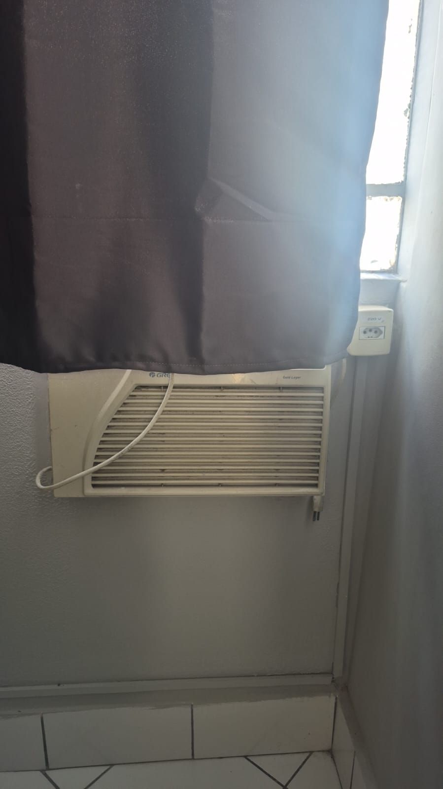 A room with a window, a white air conditioning unit, and a black curtain.