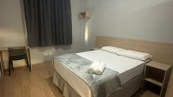 Une chambre d’hôtel bien rangée, avec un lit, une petite table de chevet, une chaise et une fenêtre avec des rideaux.