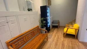 A wooden bench and a yellow chair in a hallway with lockers and a refrigerator. - Unity Hotel - Santos (Santos)