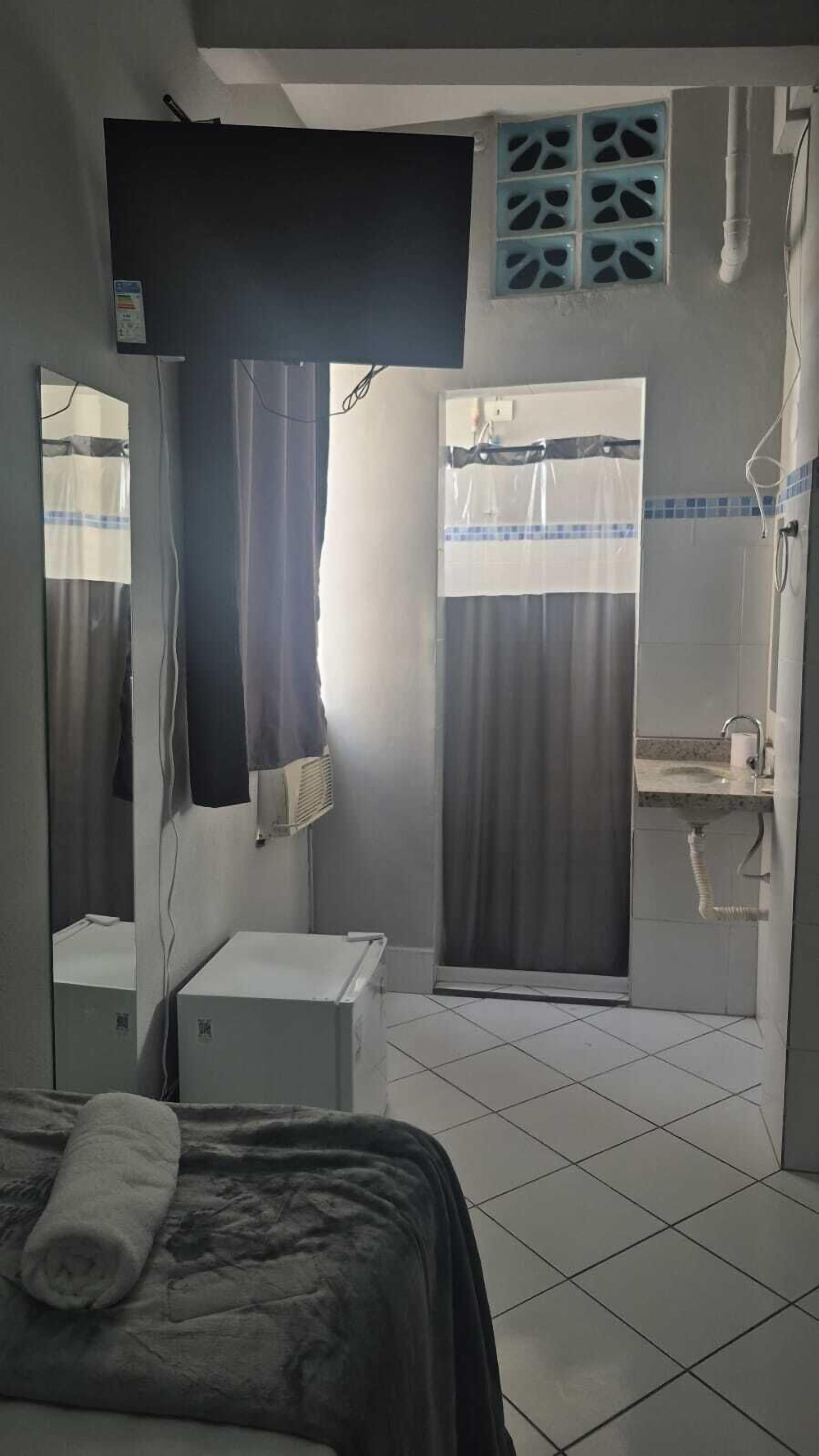 Habitación de hotel con cama, mesita de noche, espejo, ducha con cortinas y lavamanos.