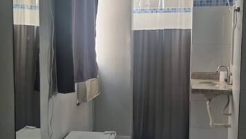 Habitación de hotel con cama, mesita de noche, espejo, ducha con cortinas y lavamanos.