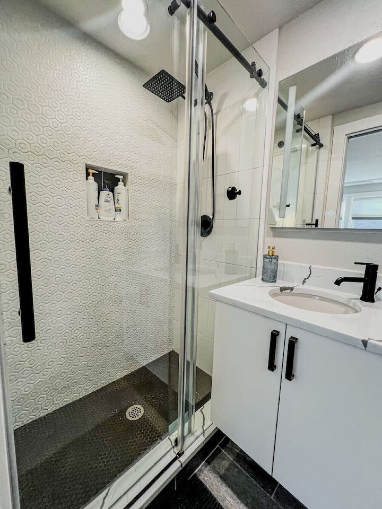 Un baño moderno con cabina de ducha de vidrio, un lavamanos blanco con grifo negro y un espejo sobre el lavamanos.