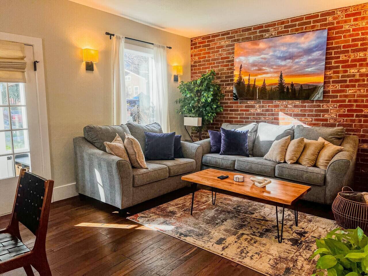 A living room with two grey sofas, a wooden coffee table, and a large painting on the brick wall.