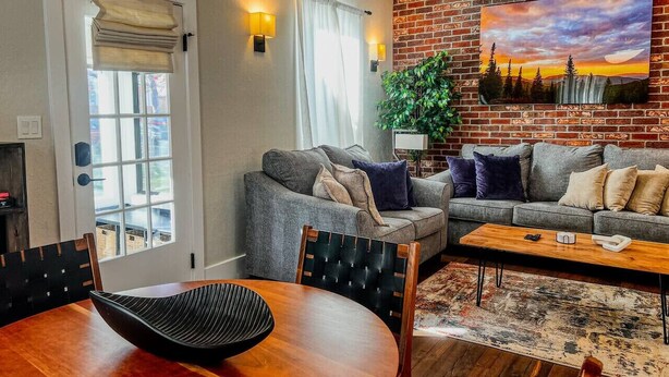 A living room with a brick wall, a painting, and a dining area with a table and chairs.