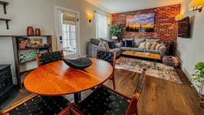 A cozy living room with a brick wall, a gray sofa, and a wooden dining table.