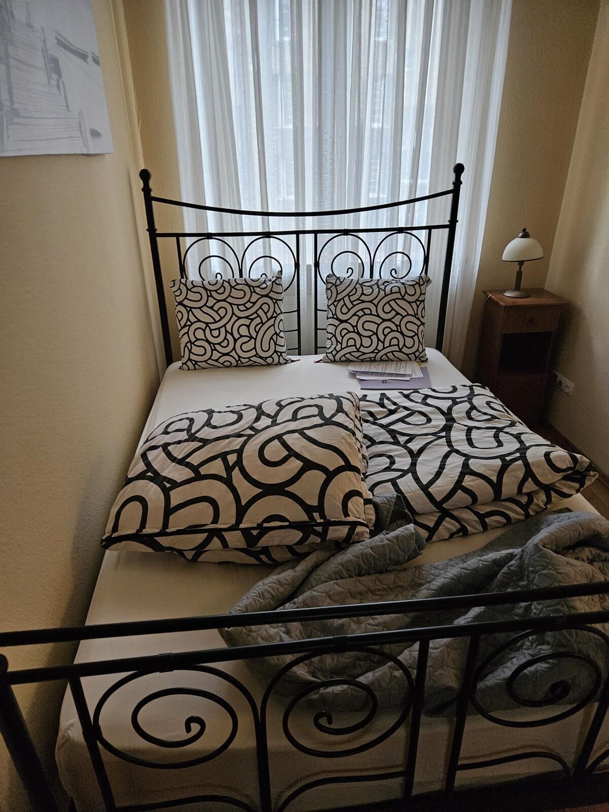 A bed with a metal frame, patterned pillows, and a bedside lamp.