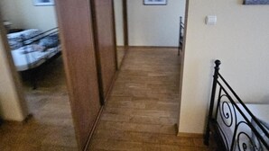 Um corredor estreito com piso de madeira que leva a um quarto com cama e janela.