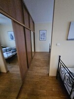 Un corridoio stretto con pavimento in legno che conduce a una camera da letto con un letto e una finestra.