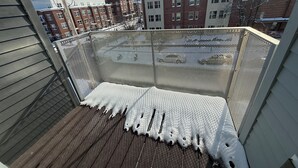 A balcony with a mesh screen, wooden floor, and a view of buildings in the background.