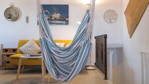 Una stanza con una poltrona amaca, un divano giallo, uno specchio tondo e un quadro incorniciato raffigurante una nave.