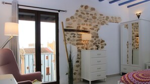 Una camera da letto con parete in pietra, un letto con copriletto decorato, una cassettiera bianca, una sedia e una lampada.