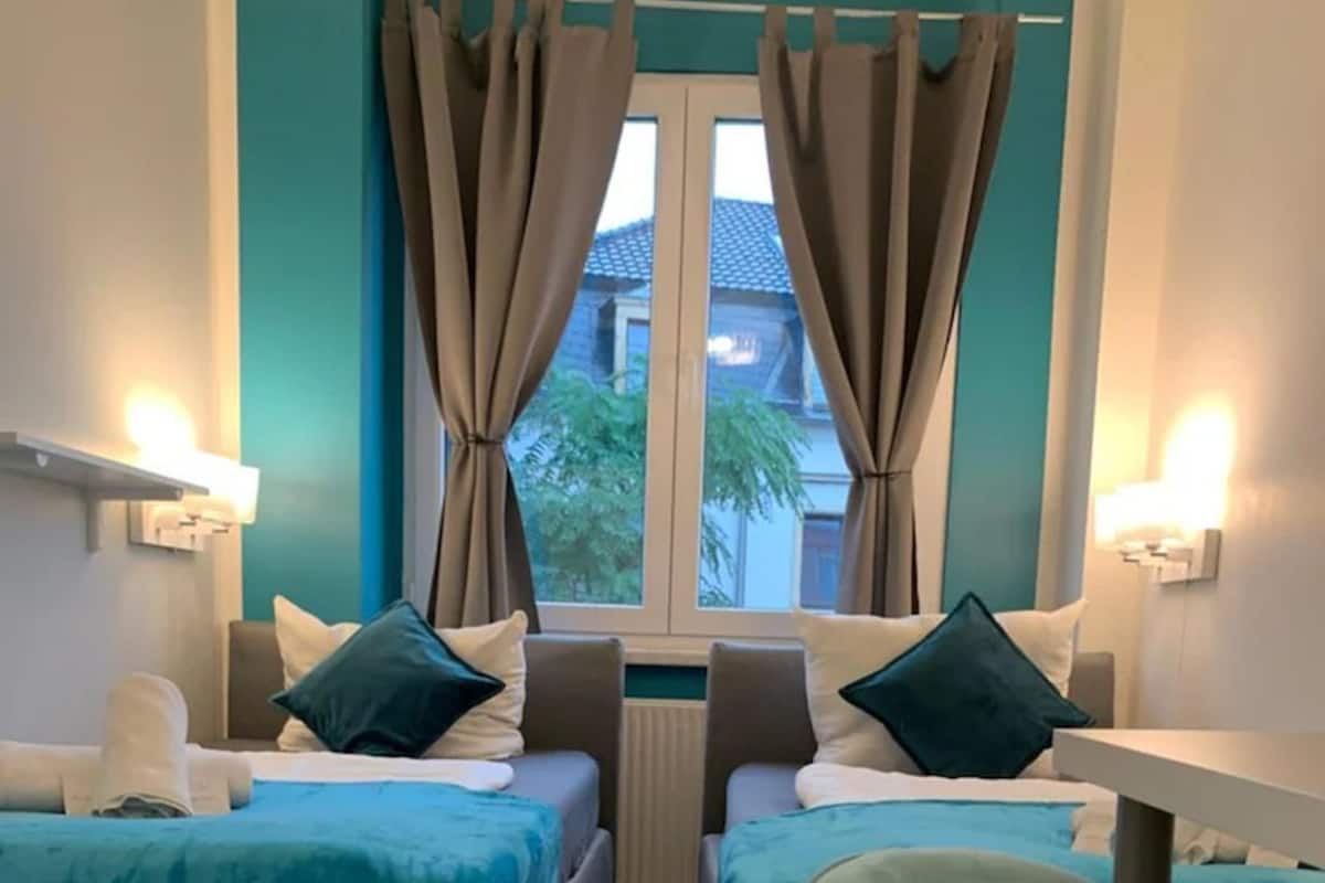 A hotel room with two beds, a window with curtains, and a view of the outside.