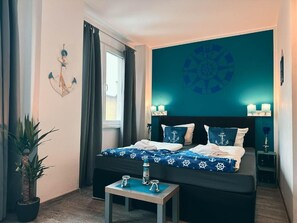 Une chambre à coucher comprenant un lit, une table de chevet, une plante en pot et un mur décoré sur le thème de la marine.