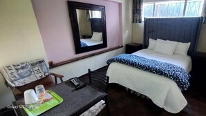 Habitación de hotel con cama, mesita de noche con lámpara, una silla, una pequeña mesa con bandeja y un espejo en la pared.