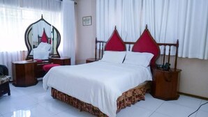 Un dormitorio ordenado con una cama grande, una mesita de noche, un espejo y una silla.