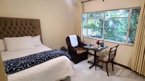 Habitación de hotel con una cama grande, una mesa pequeña con una silla, un televisor montado en la pared y una ventana con vistas a zonas verdes.