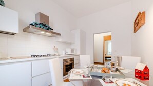 Une cuisine moderne avec des meubles blancs, une cuisinière à gaz, un four à micro-ondes et une décoration rouge en forme de maison posée sur la table.