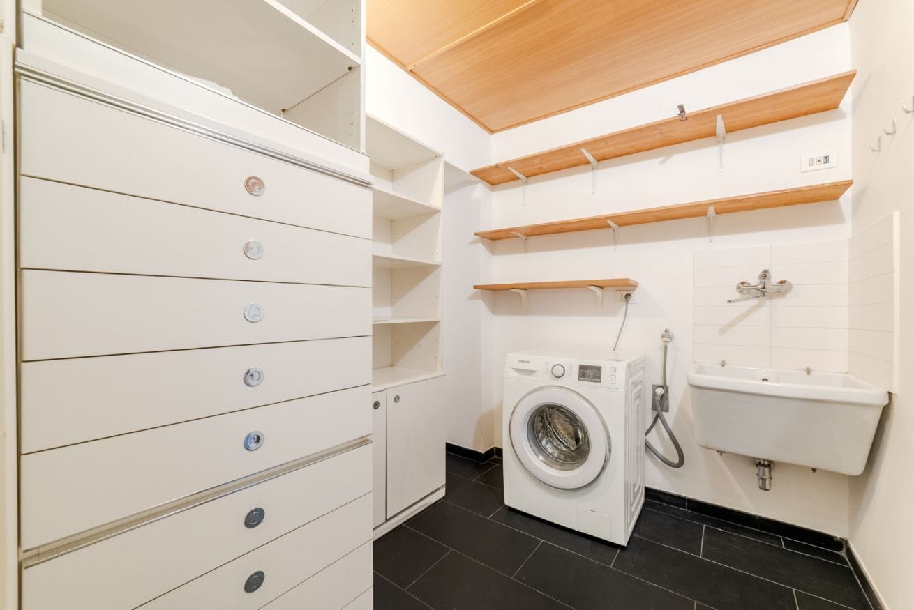 Een wasserette met een wasmachine, een wasbak en opbergkasten.