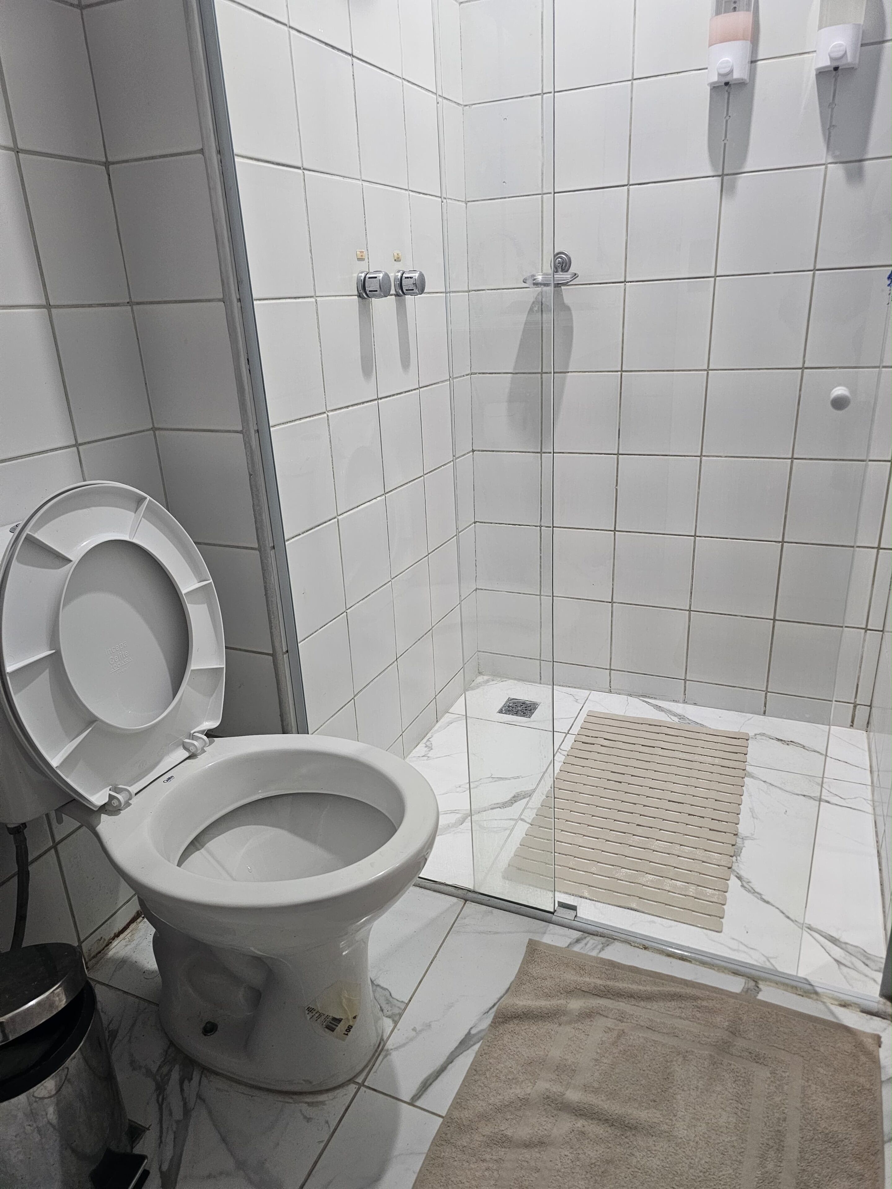 Um banheiro com vaso sanitário, chuveiro e piso revestido de azulejos.