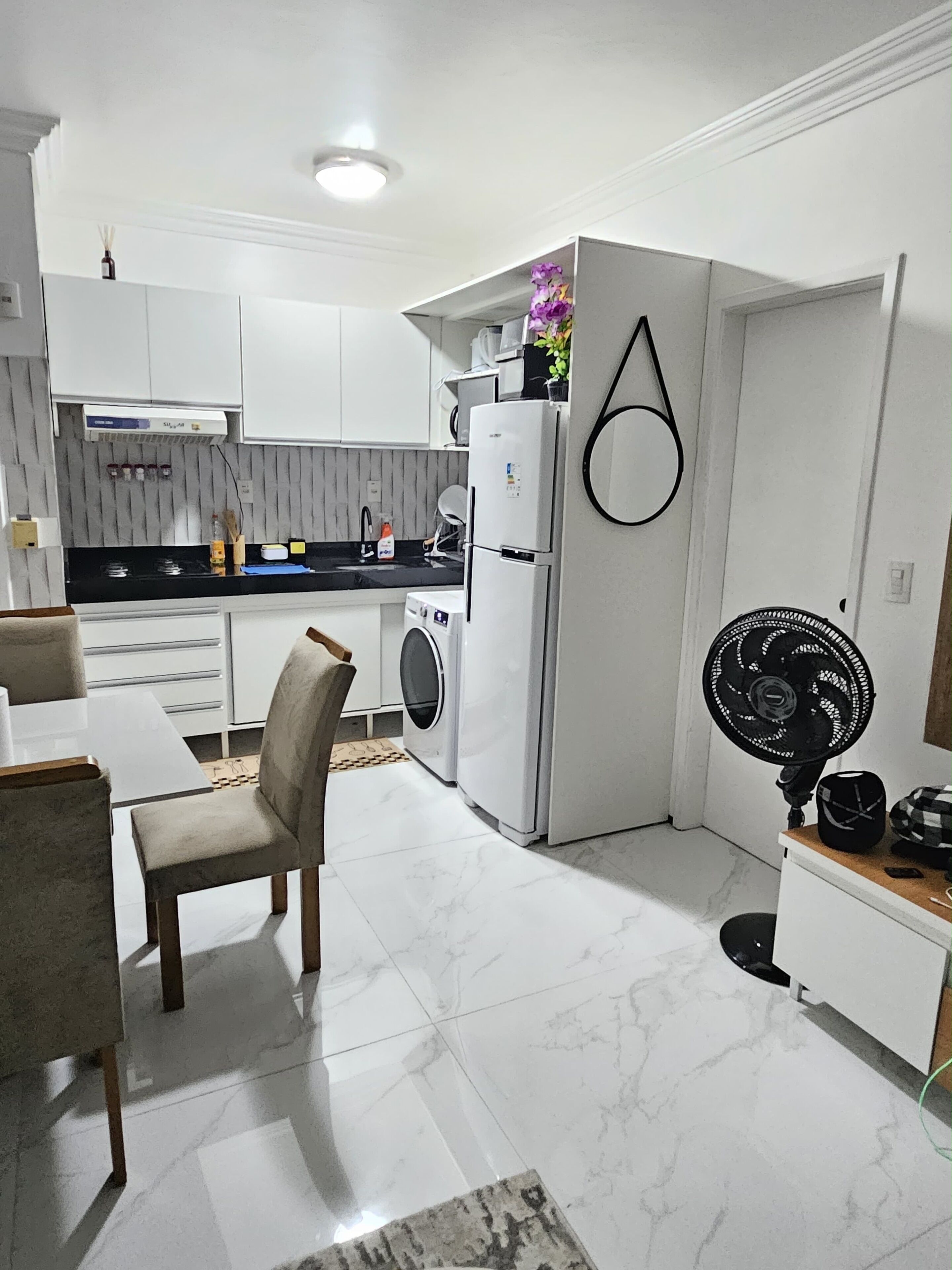 Uma cozinha compacta com máquina de lavar, geladeira e ventilador.