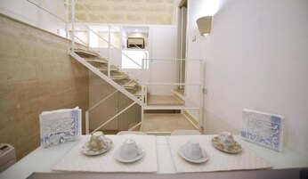 Una camera d'albergo con una scala, un tavolo da pranzo apparecchiato con piatti e tazze, e uno scaffale a parete con oggetti decorativi.