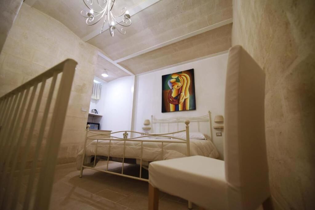 A bedroom with a bed, a chair, a painting on the wall, and a chandelier.