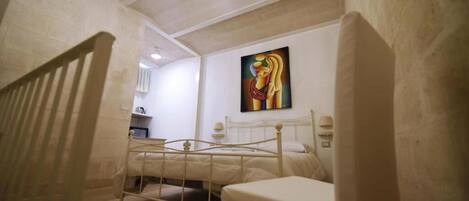 A bedroom with a bed, a chair, a painting on the wall, and a chandelier.
