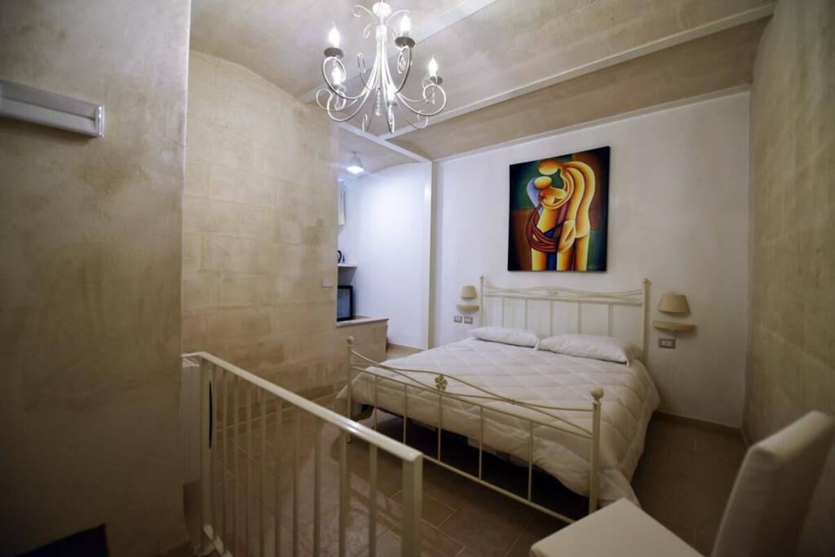 Une chambre à coucher avec un lit, un lustre, un tableau au mur et une table de chevet.