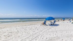A beach with white sand, blue umbrellas, and beach chairs. - NEW Sea Glass 415 • Balcony • Pool & Ocean Views • Walk to Hangout (Gulf Shores)